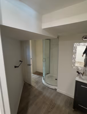 A bright, empty room with white walls, light wooden floors, and a partially visible doorway leading to another space.