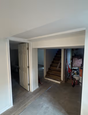 Another angle of the empty room, highlighting the white walls, light wooden floors, and a glimpse into an adjacent area.